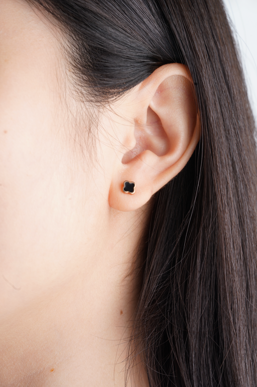 Close-up of an ear with a black earring against a neutral background