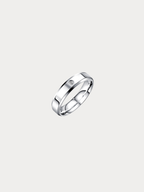 A polished silver band ring with a small, round clear gemstone set on the upper left side, shown against a solid light gray background.
