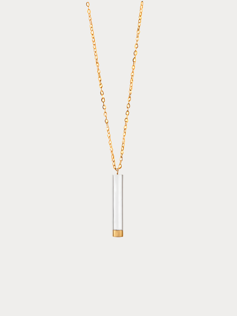 A delicate gold chain necklace featuring a minimalist cylindrical pendant with a white center and a gold-toned base, displayed against a light gray background.