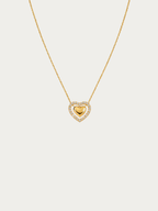 A delicate gold chain necklace featuring a heart-shaped pendant with a polished gold center heart surrounded by a halo of small clear stones, set against a solid light gray background.