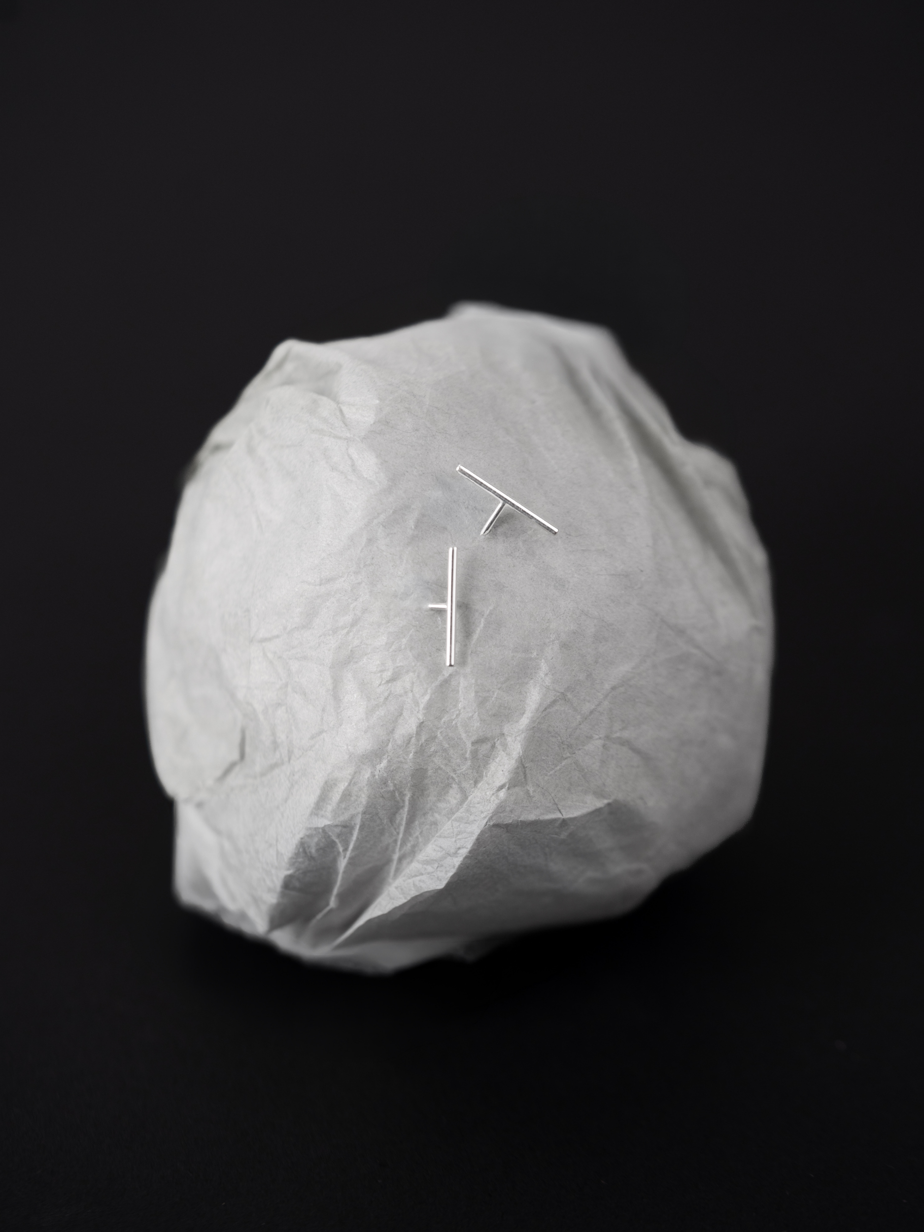 Alaia Minimalist Bar Stud Earrings styled on crumpled paper backdrop