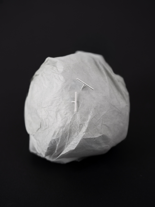 Alaia Minimalist Bar Stud Earrings styled on crumpled paper backdrop