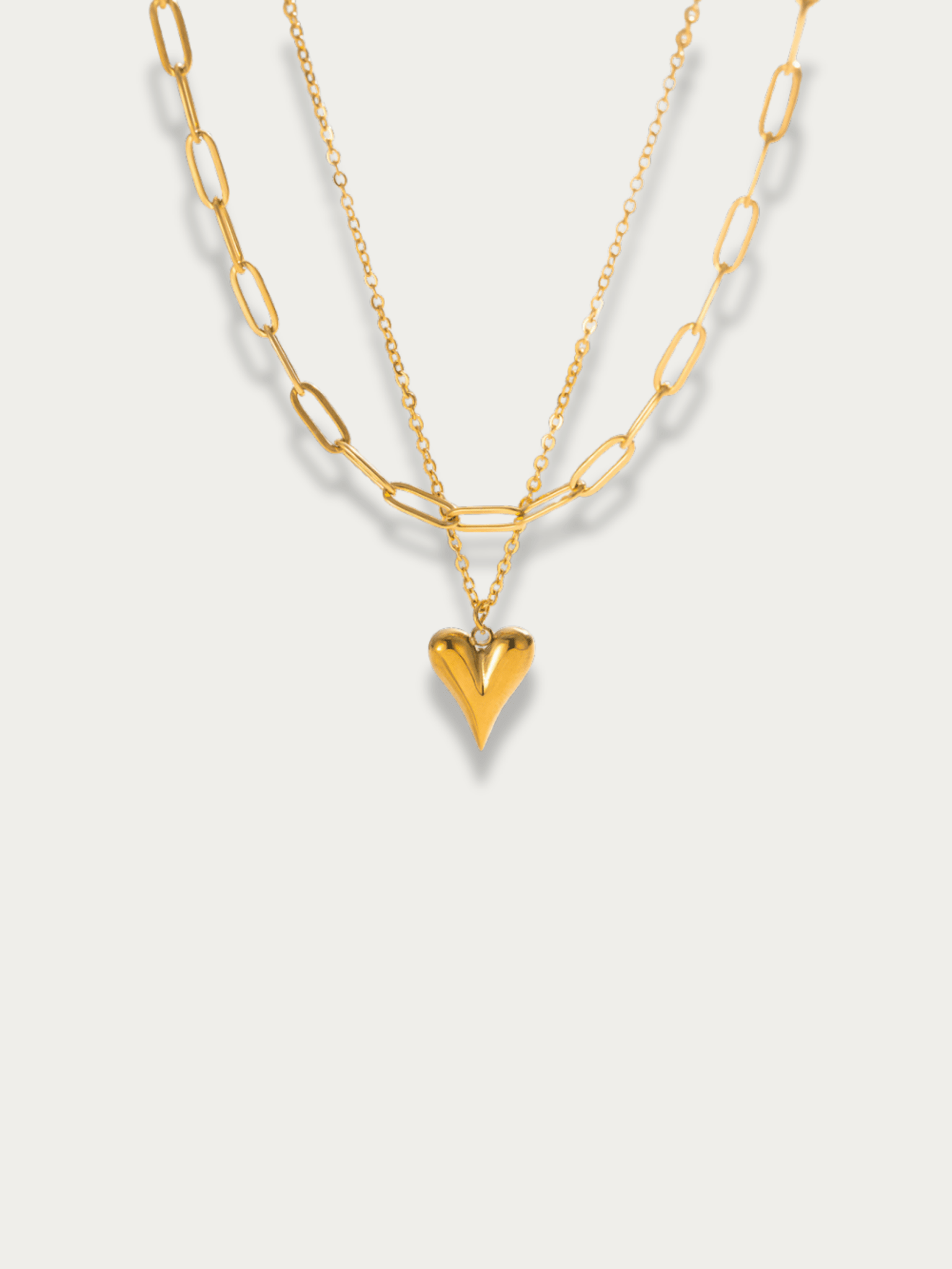 Amora Double Layered Necklace in gold titanium with paperclip chain, fine chain, and heart pendant, studio hero shot