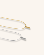 Flat lay of Axis Pendant Wheat Chain Necklace in silver and gold