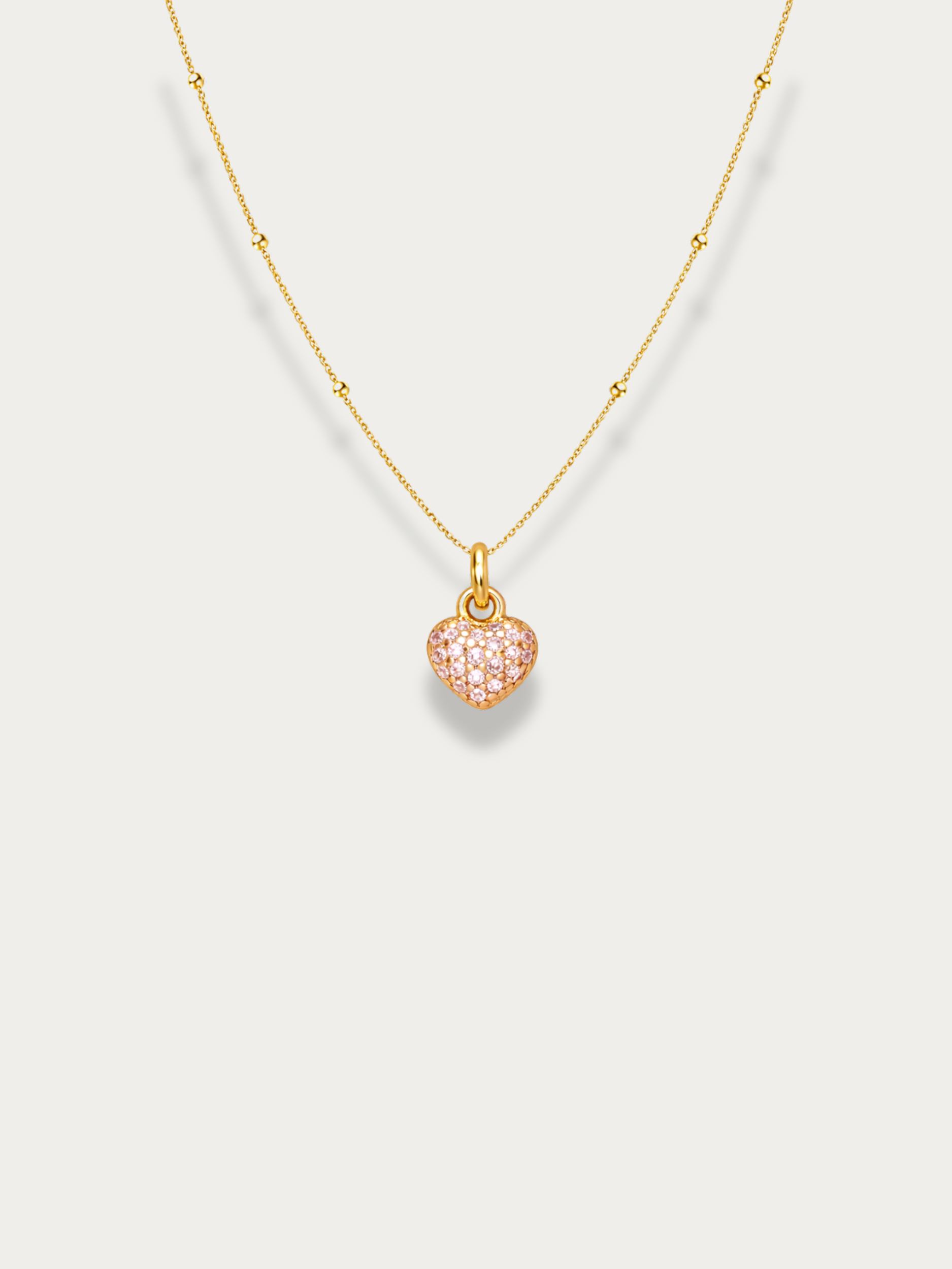 Gold necklace with a heart-shaped pink gemstone pendant on a light gray background