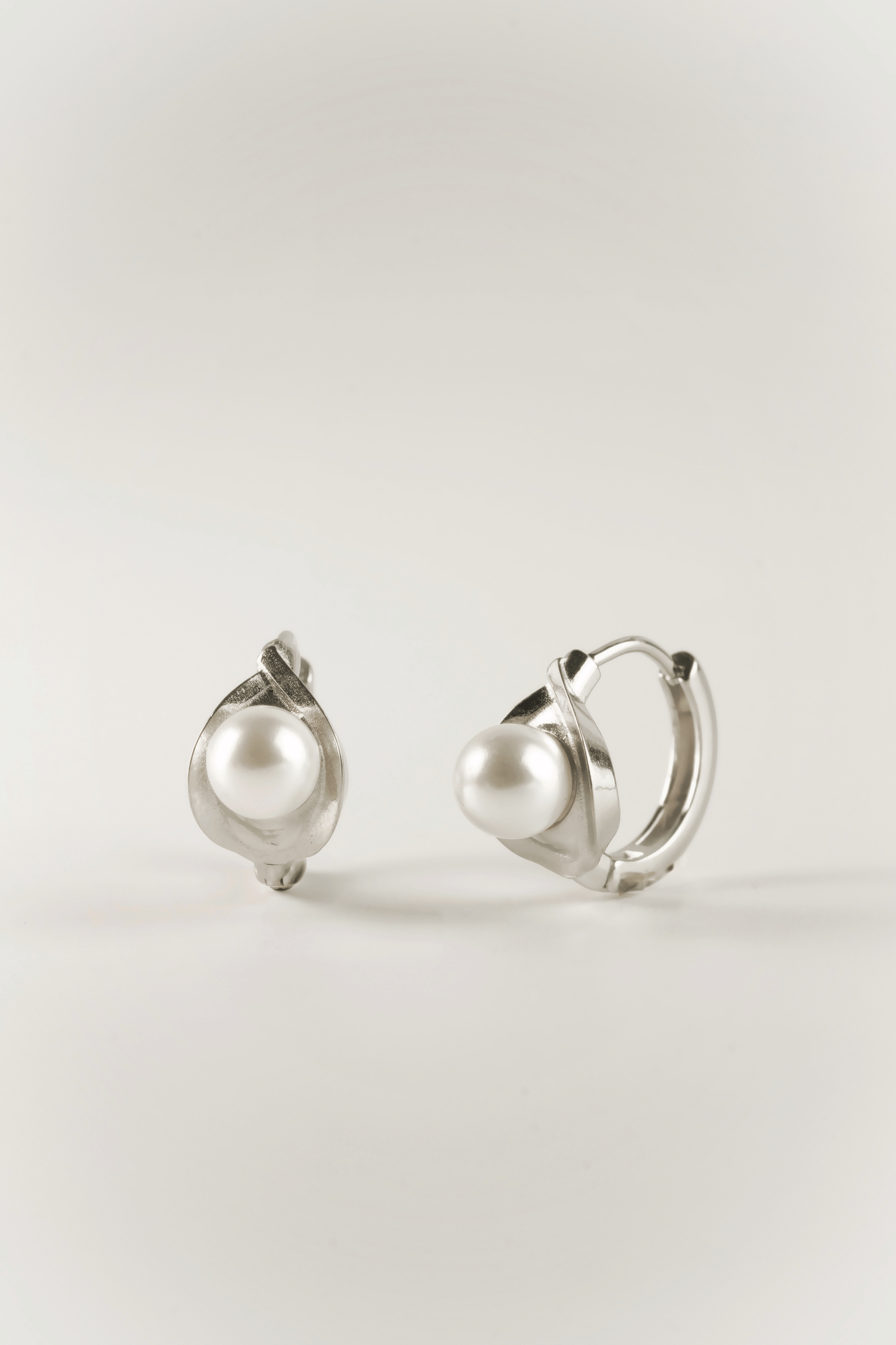 Carina Pearl Huggie Earrings in silver tone stainless steel, sculptural pearl huggie product flatlay