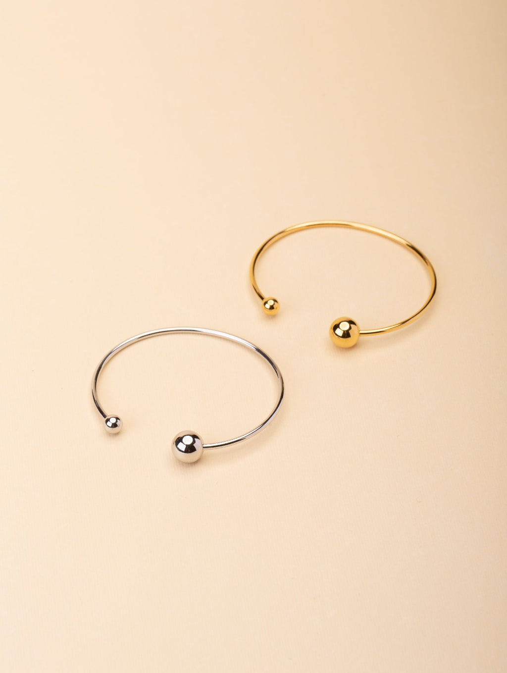 Enso Orbital Bangle gold and silver tone stainless steel, open cuff with asymmetric ball ends, product flatlay