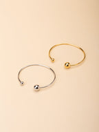 Enso Orbital Bangle gold and silver tone stainless steel, open cuff with asymmetric ball ends, product flatlay