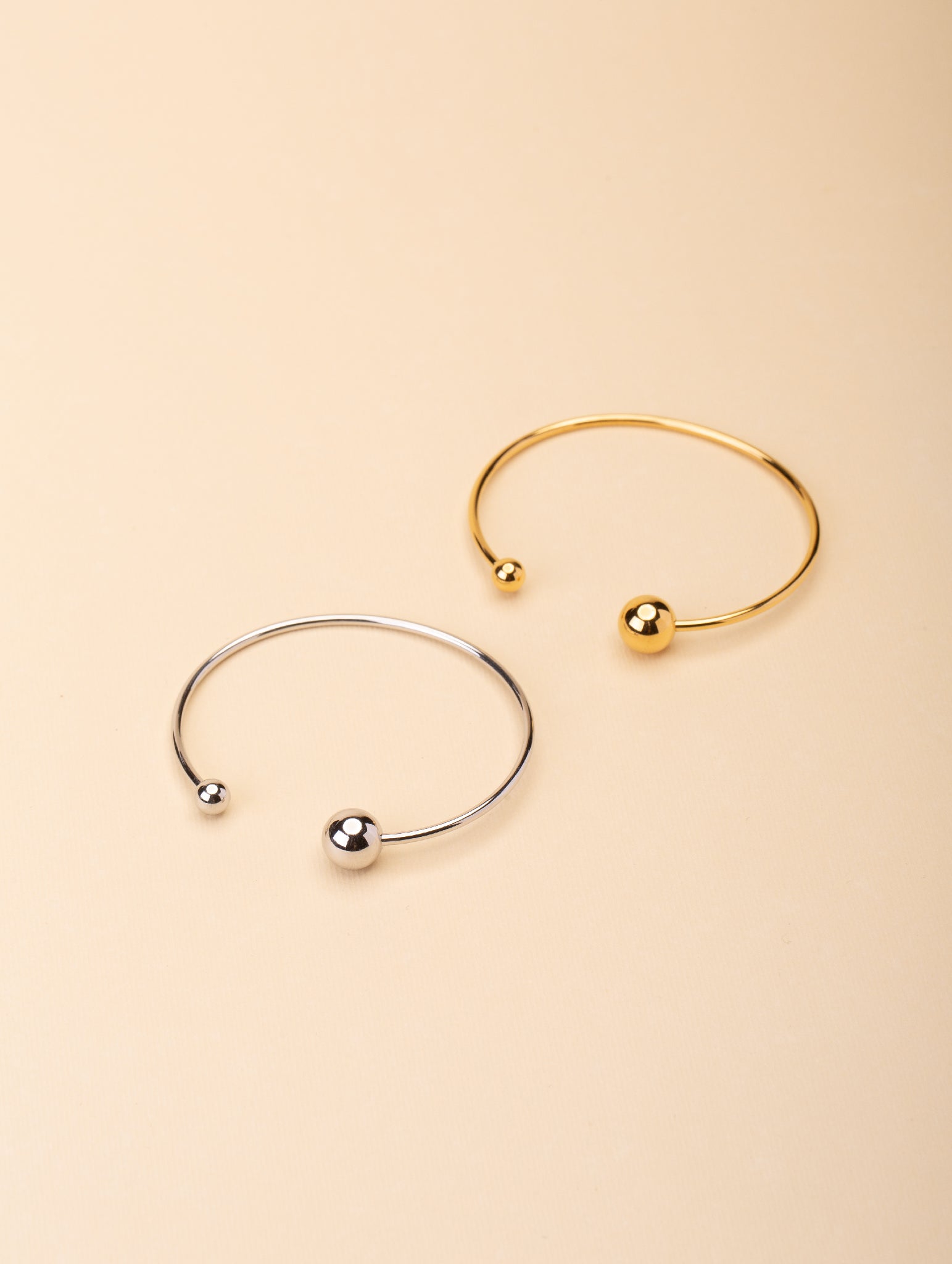 Enso Orbital Bangle gold and silver tone stainless steel, open cuff with asymmetric ball ends, product flatlay