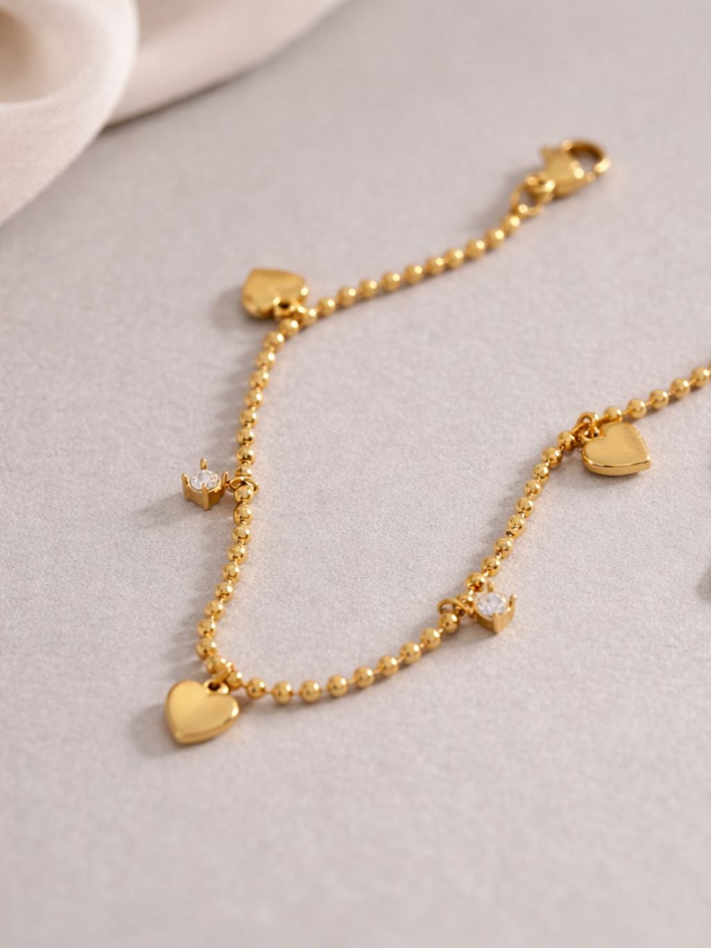 Detail of alternating heart and CZ charms on Jaye Heart Charm Bracelet bead chain, gold tone