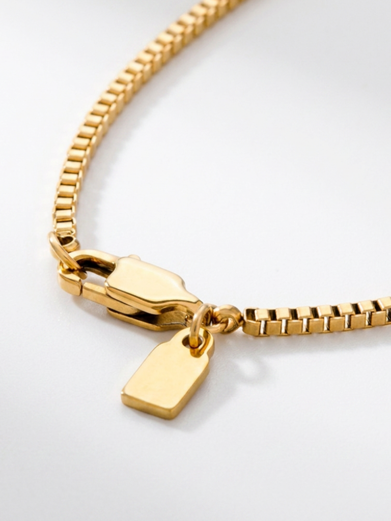 Macro detail of Minimalist Box Chain Necklace lobster clasp and MNML tag in gold