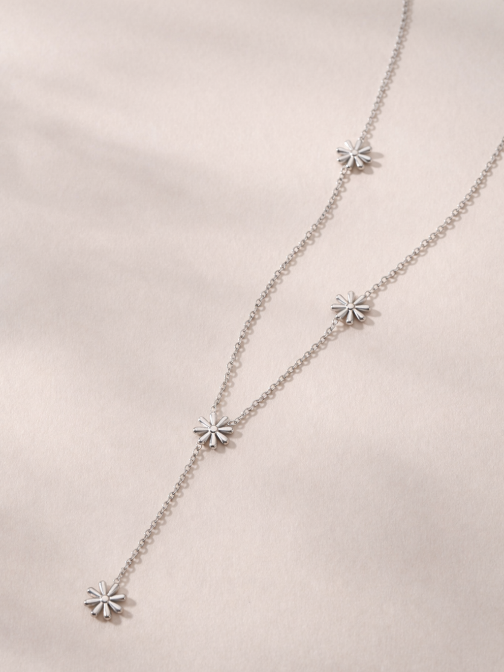 MNML Elia Daisy Lariat Necklace in silver and gold flat lay — stainless steel daisy jewelry
