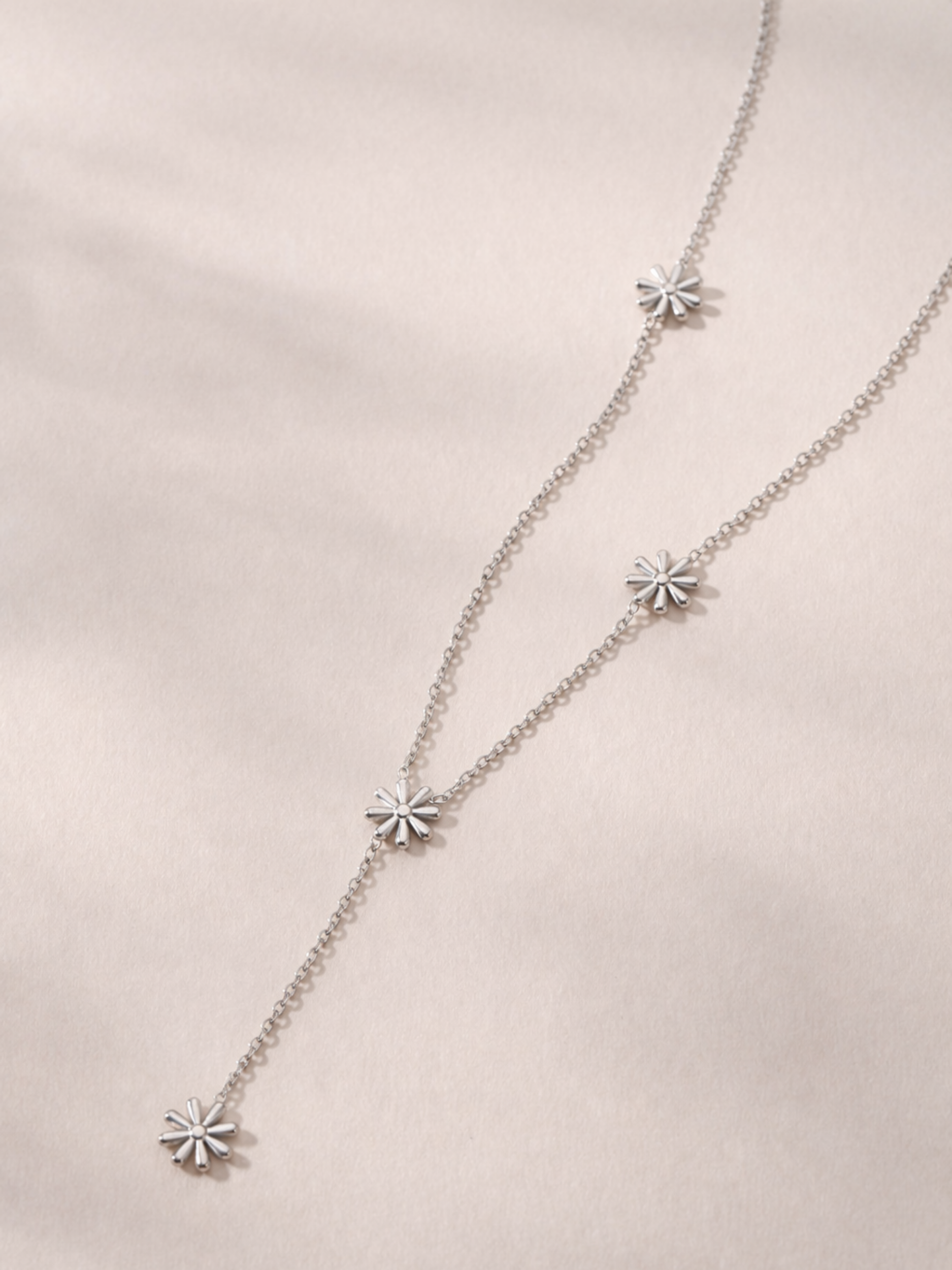 MNML Elia Daisy Lariat Necklace in silver and gold flat lay — stainless steel daisy jewelry