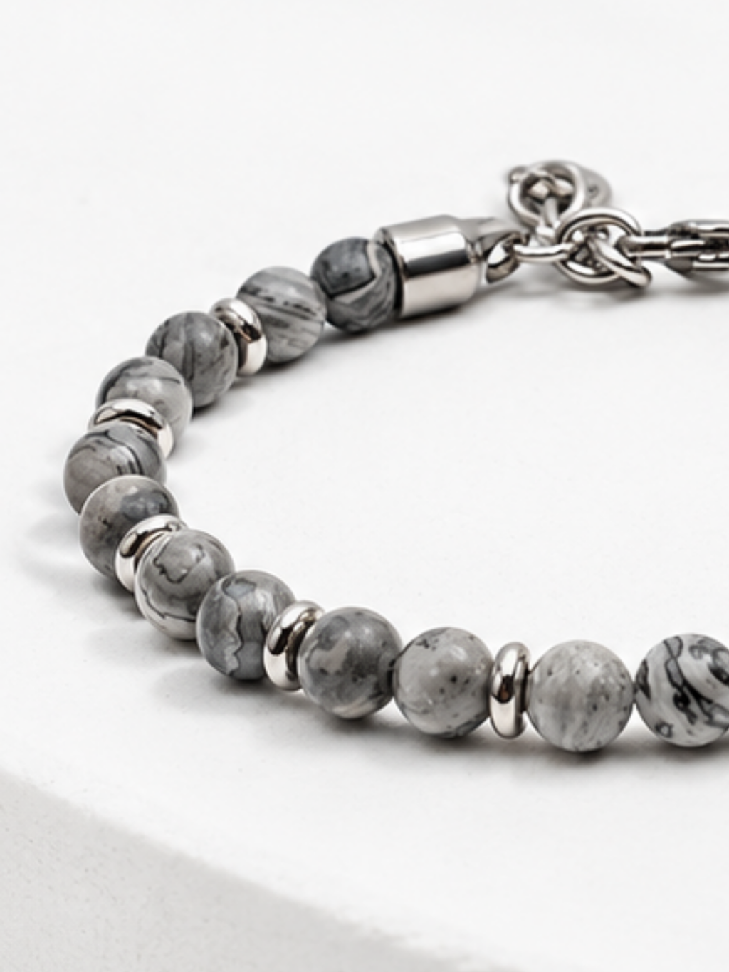 Close-up of grey map stone beads with charcoal veining beside a polished steel end cap and the clasp