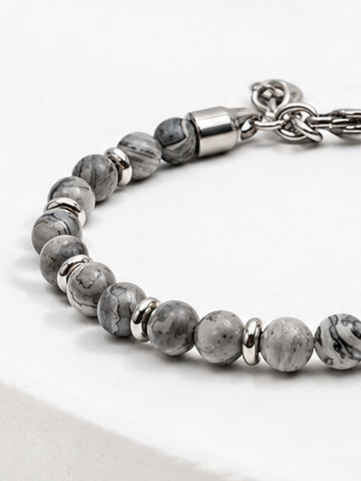 Close-up of grey map stone beads with charcoal veining beside a polished steel end cap and the clasp