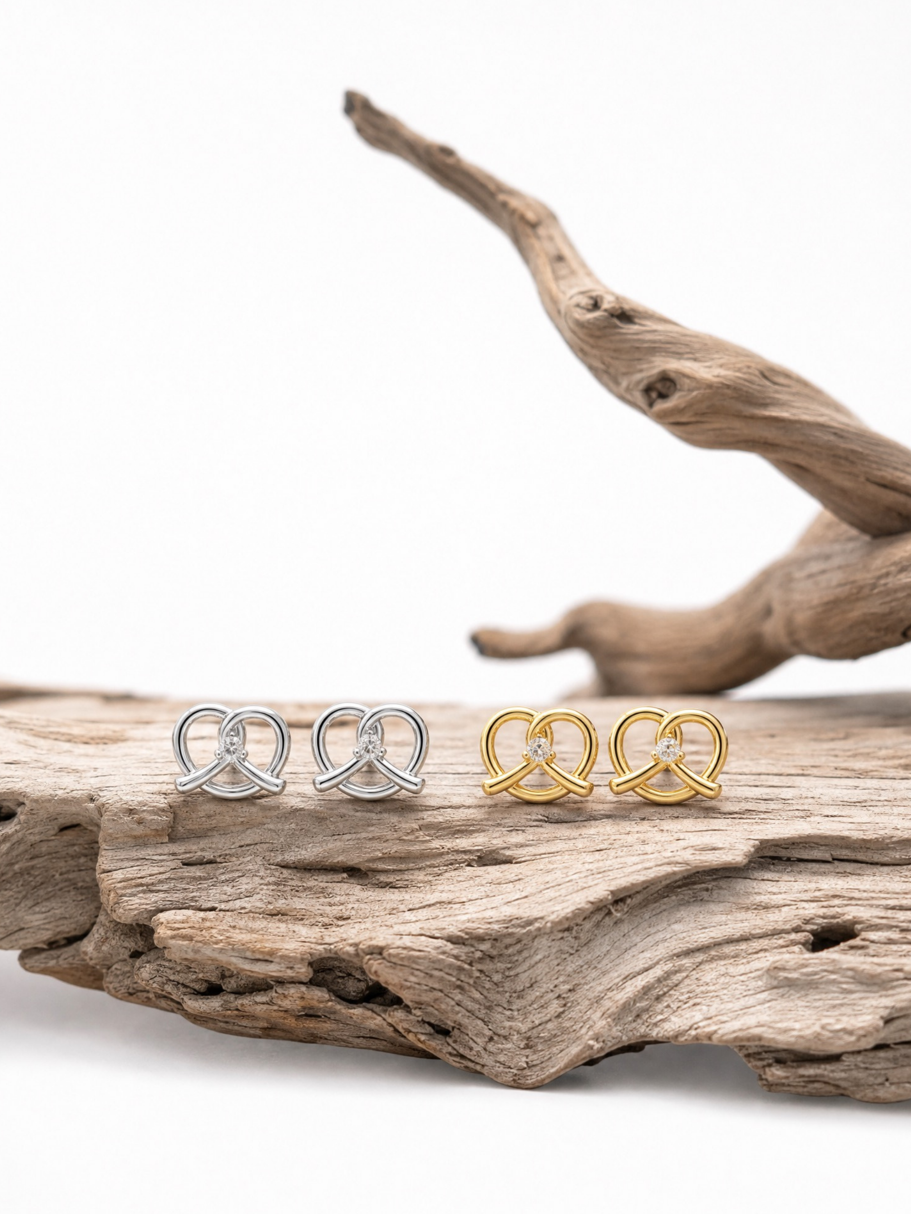 MNML Little Pretzel Stud Earrings in silver and gold flat lay — titanium CZ pretzel earrings