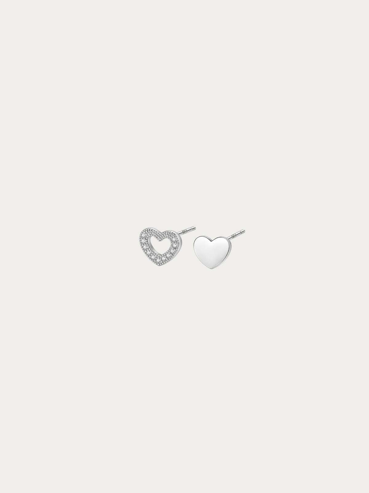 Teeny Tiny asymmetrical heart stud pair in rhodium-plated 925 silver, with an open pavé heart and a solid heart side by side