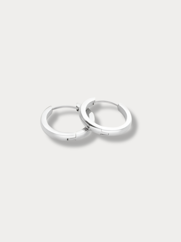 A pair of polished silver huggie hoop earrings resting on a light gray background.