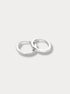 A pair of polished silver huggie hoop earrings resting on a light gray background.